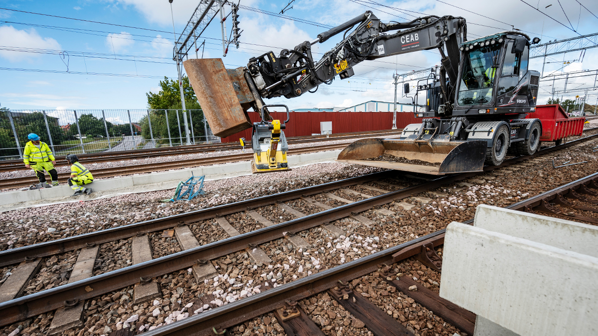 Banarbete pågår, del av järnväg med människor och en stor maskin.