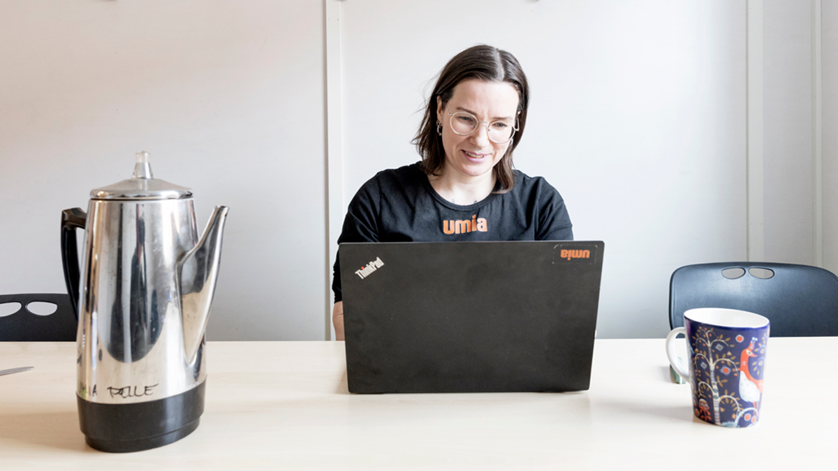 Ellen Brännvall framför datorn, omgiven av en perkolator och en pappmugg.