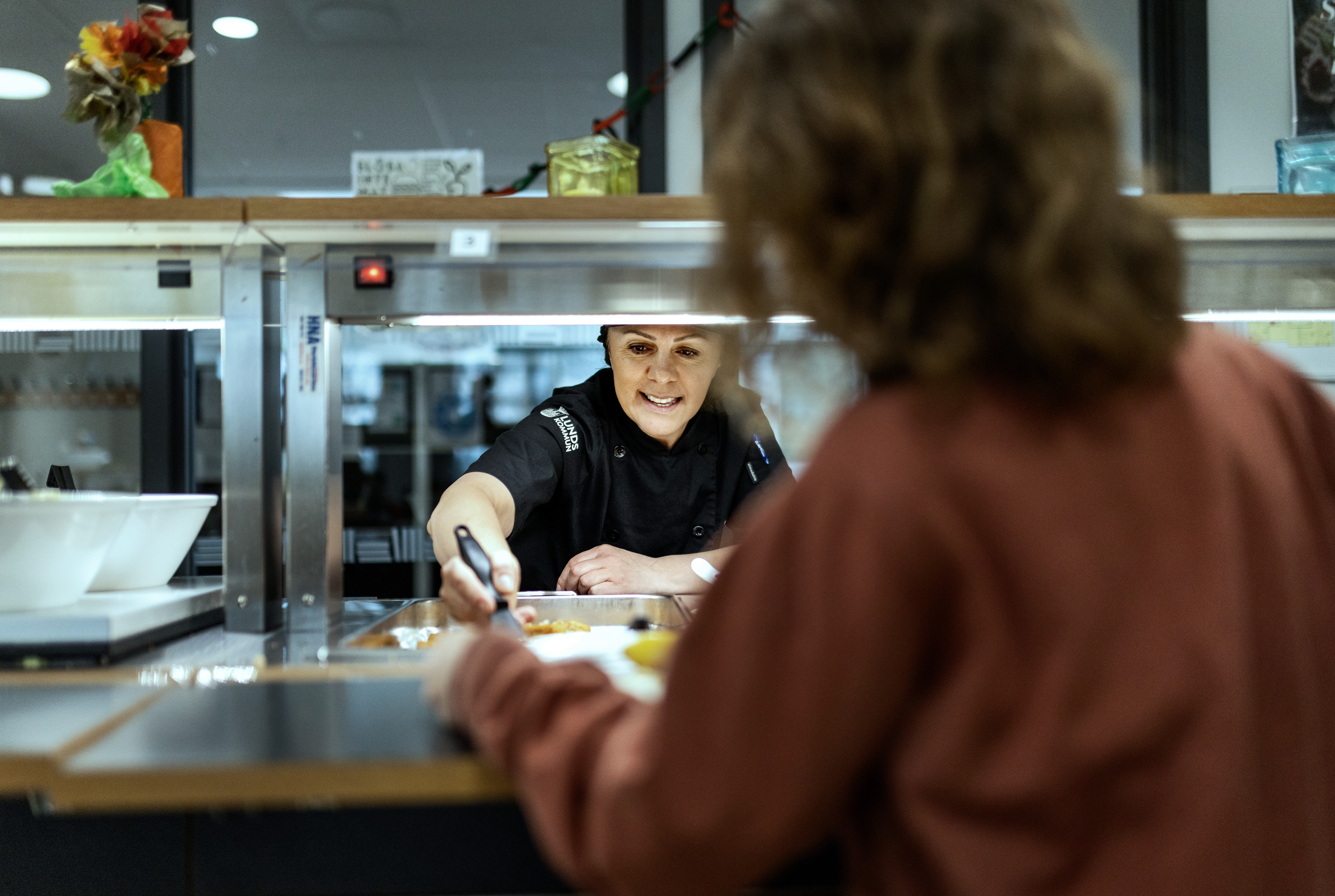 Flora Shahini assisterar när eleverna kommer in för att äta lunch.