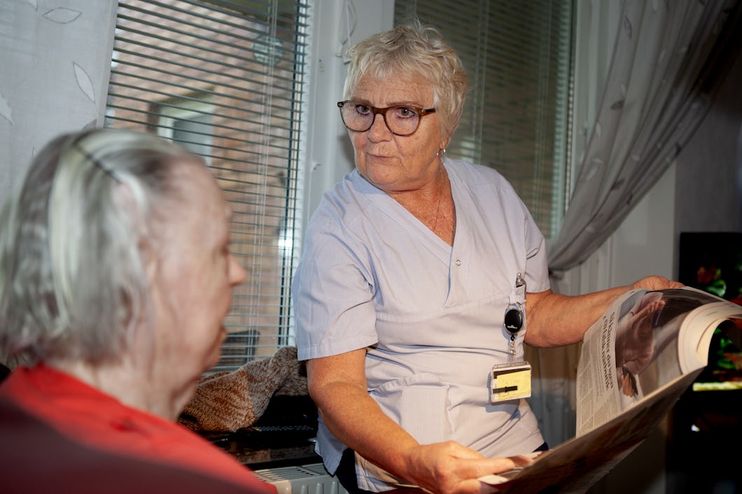 Britt-Marie Haraldsson på hemtjänsten i Halmstad läser tidningen för brukaren Majken Jansson.
