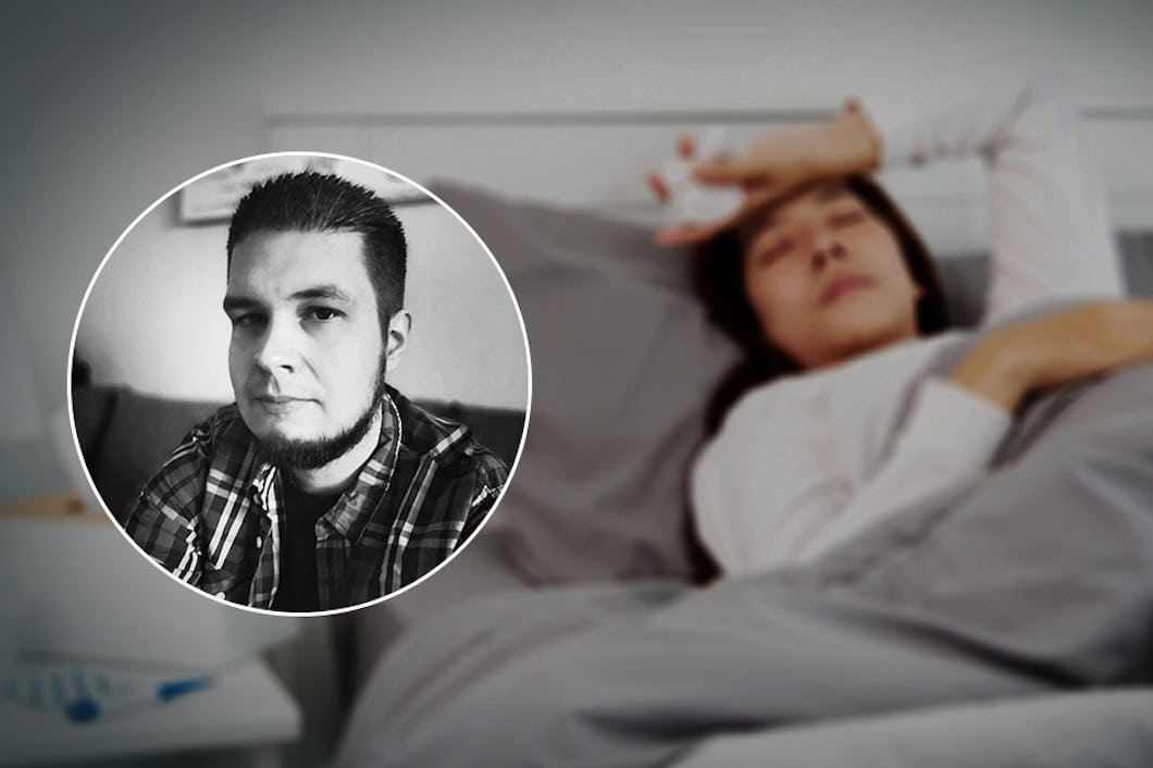 Kvinna ligger sjuk i sängen och håller sig för pannan