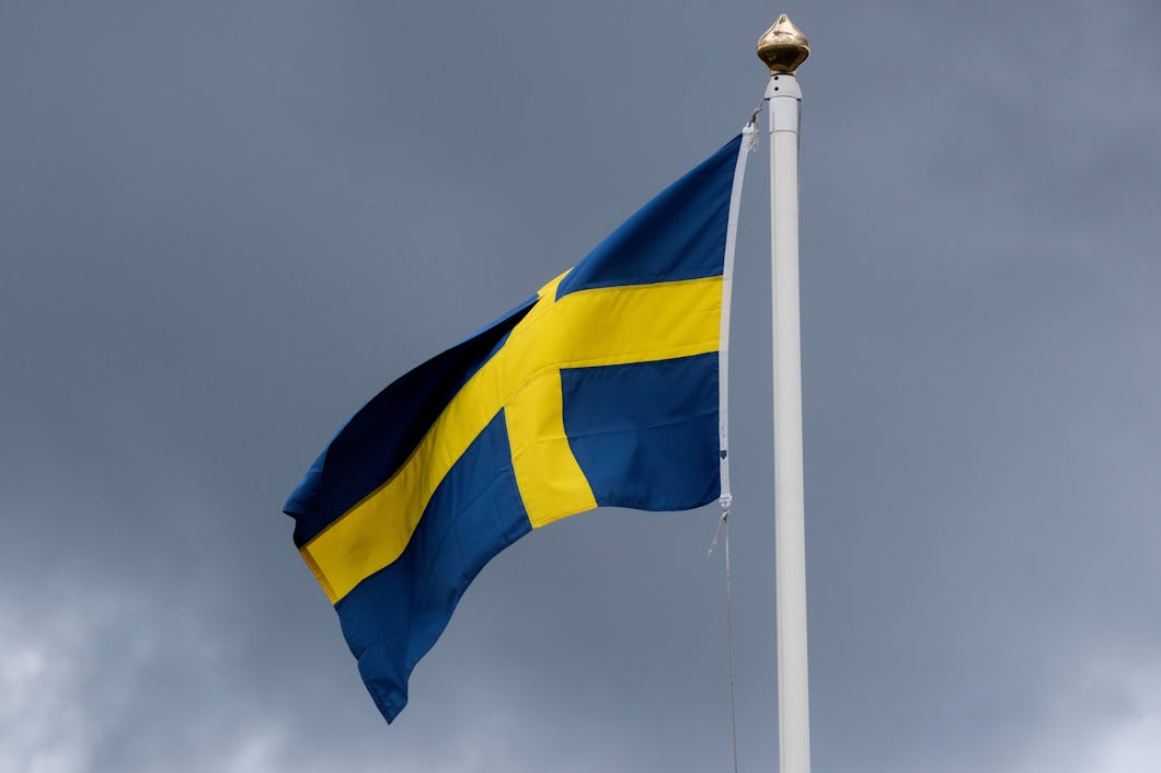 En svensk flagga vajar framför en molnig himmel.