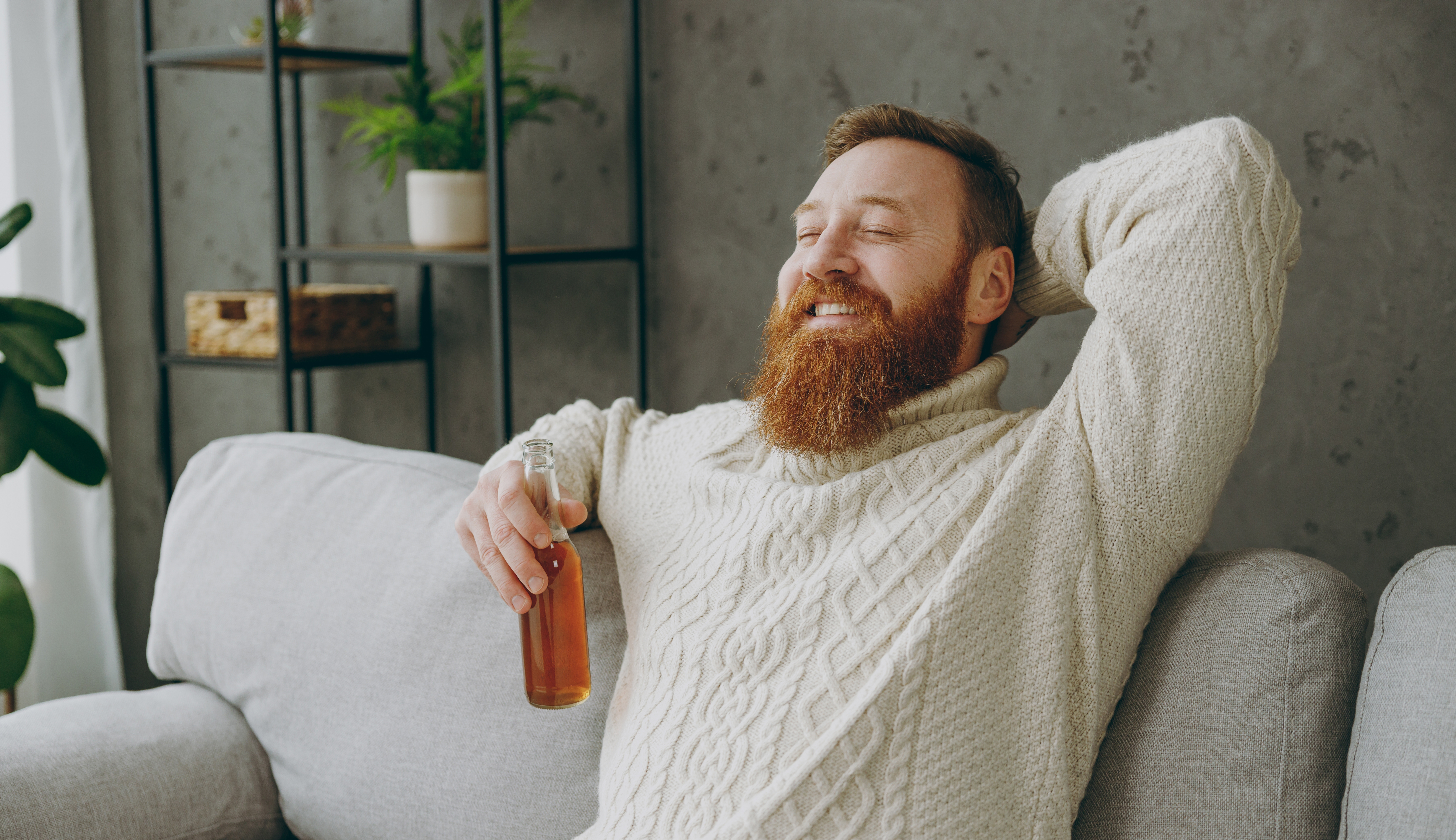 En skäggig man sitter i en soffa med en flaska.