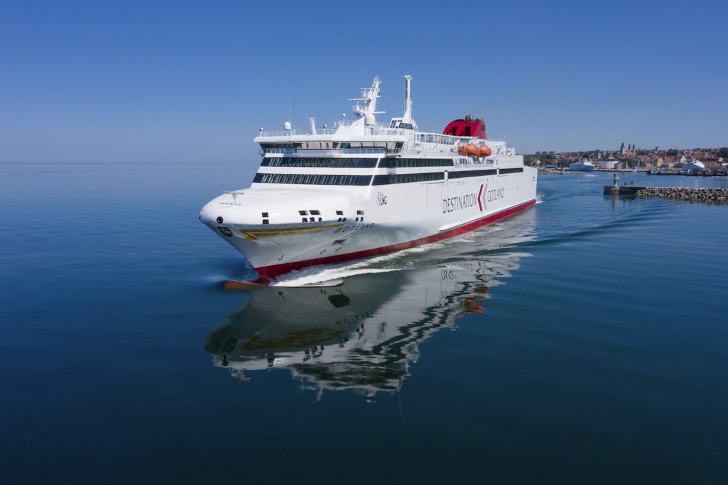 En vit och röd färja från Destination Gotland färdas över Östersjön med Visby i bakgrunden.
