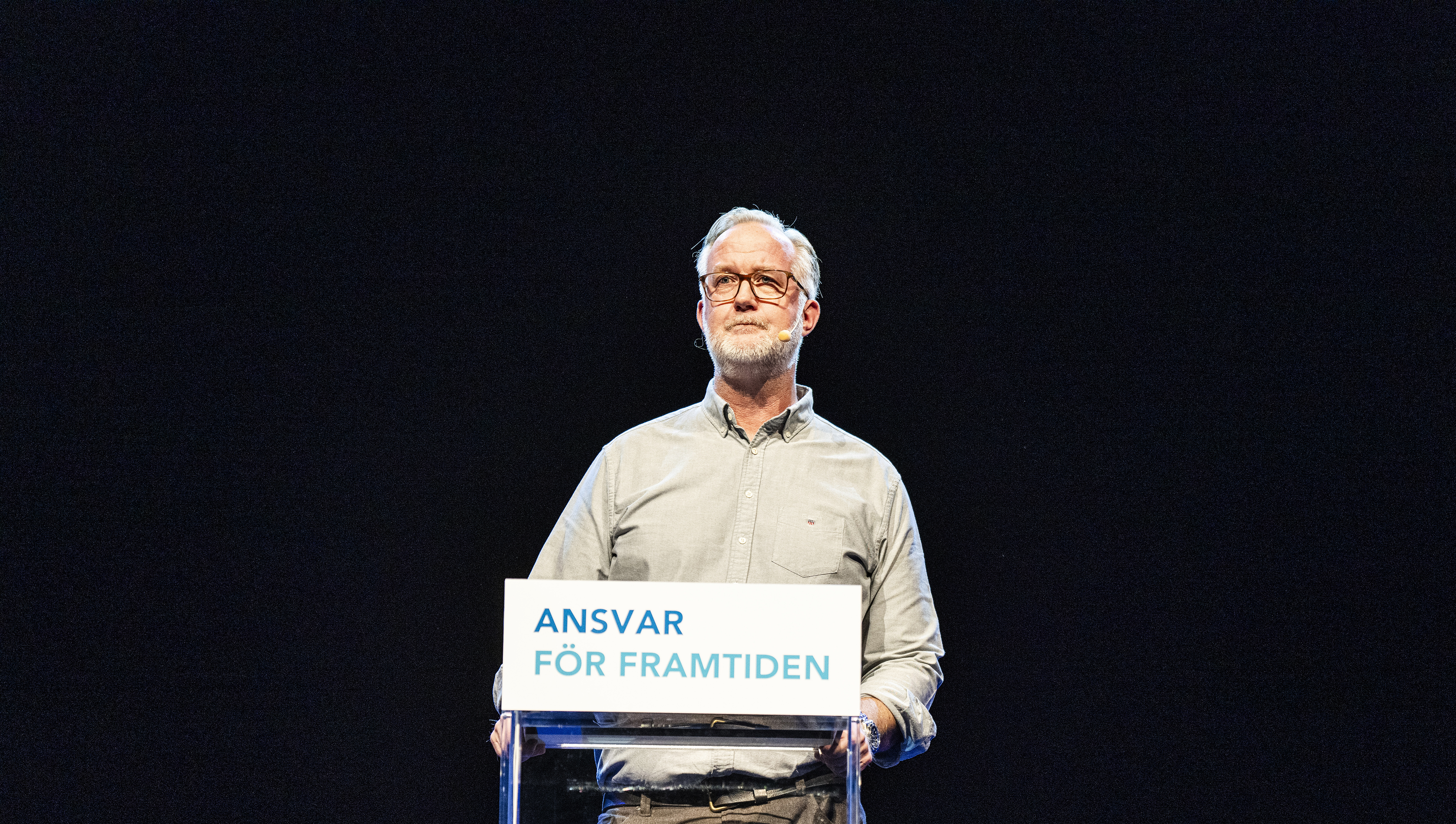 Johan Pehrson står på ett podium framför en svart skärm.