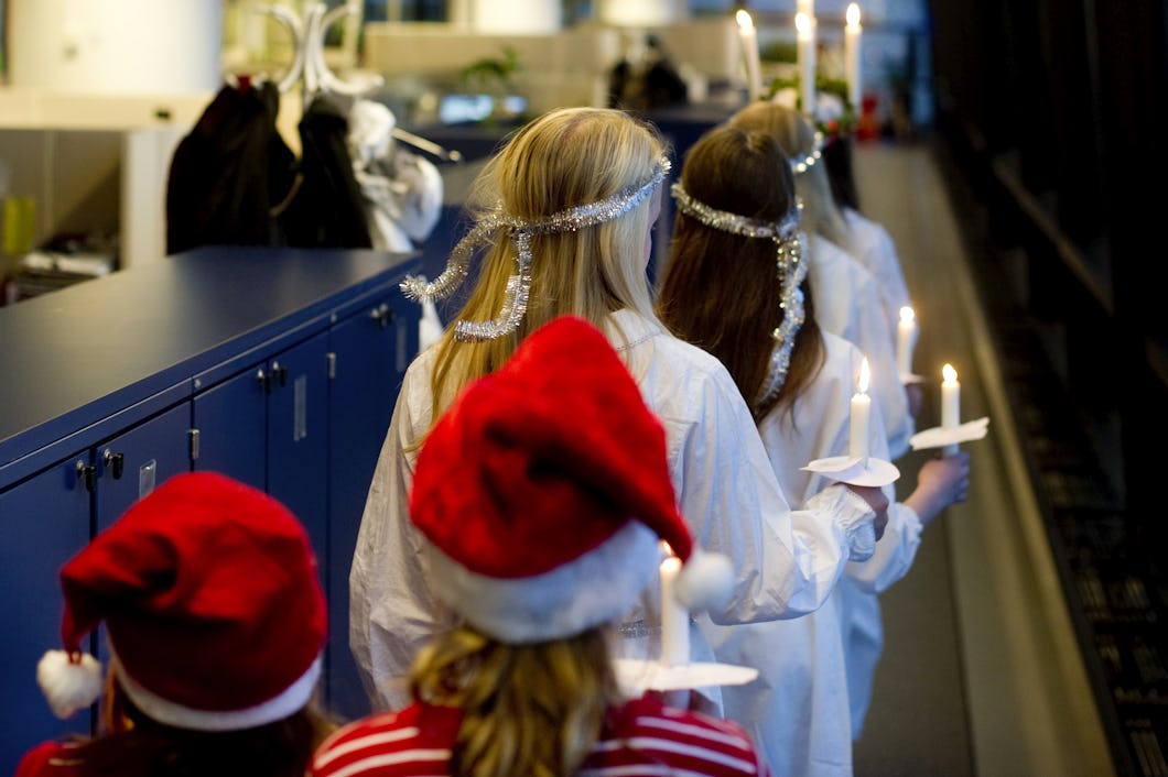 En grupp barn i tomtehattar och glitter som håller ljus på ett kontor.