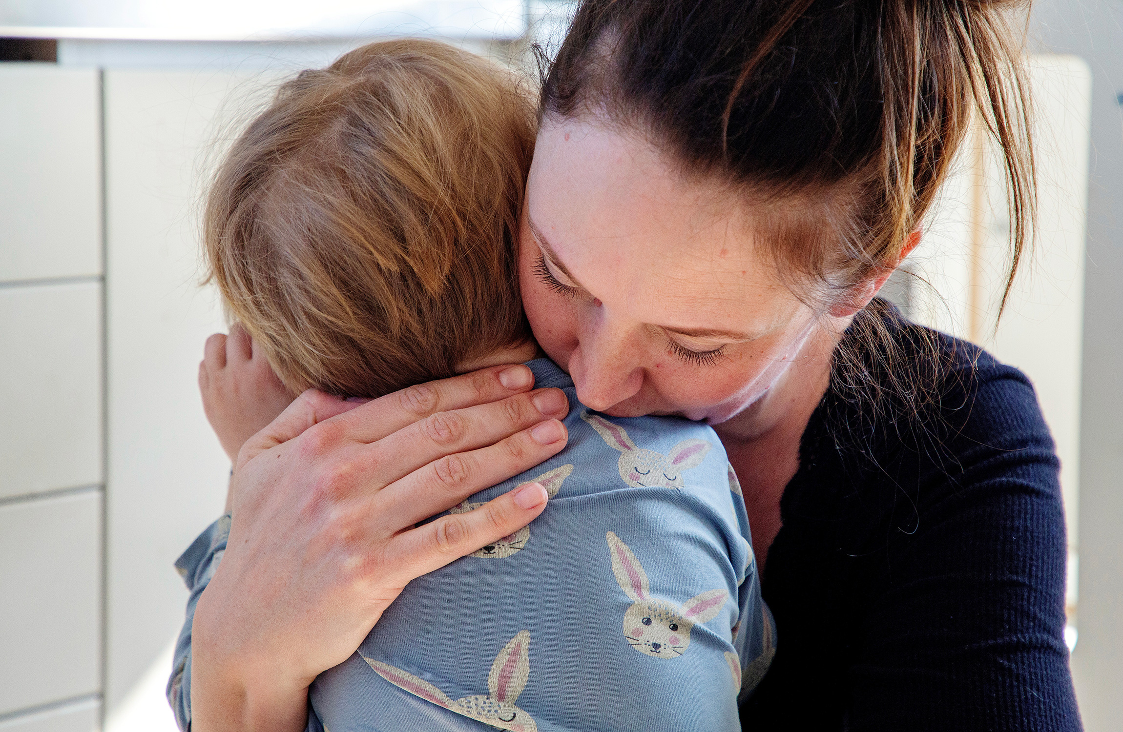 En kvinna kramar ett barn i ett kök.