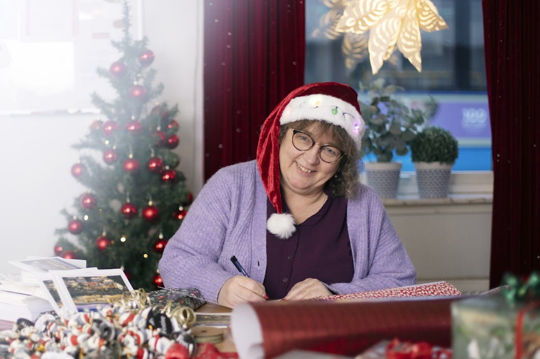 Mona Burås Dieng i en tomtehatt som sitter vid ett skrivbord och slår in julklappar till sina kollegor.