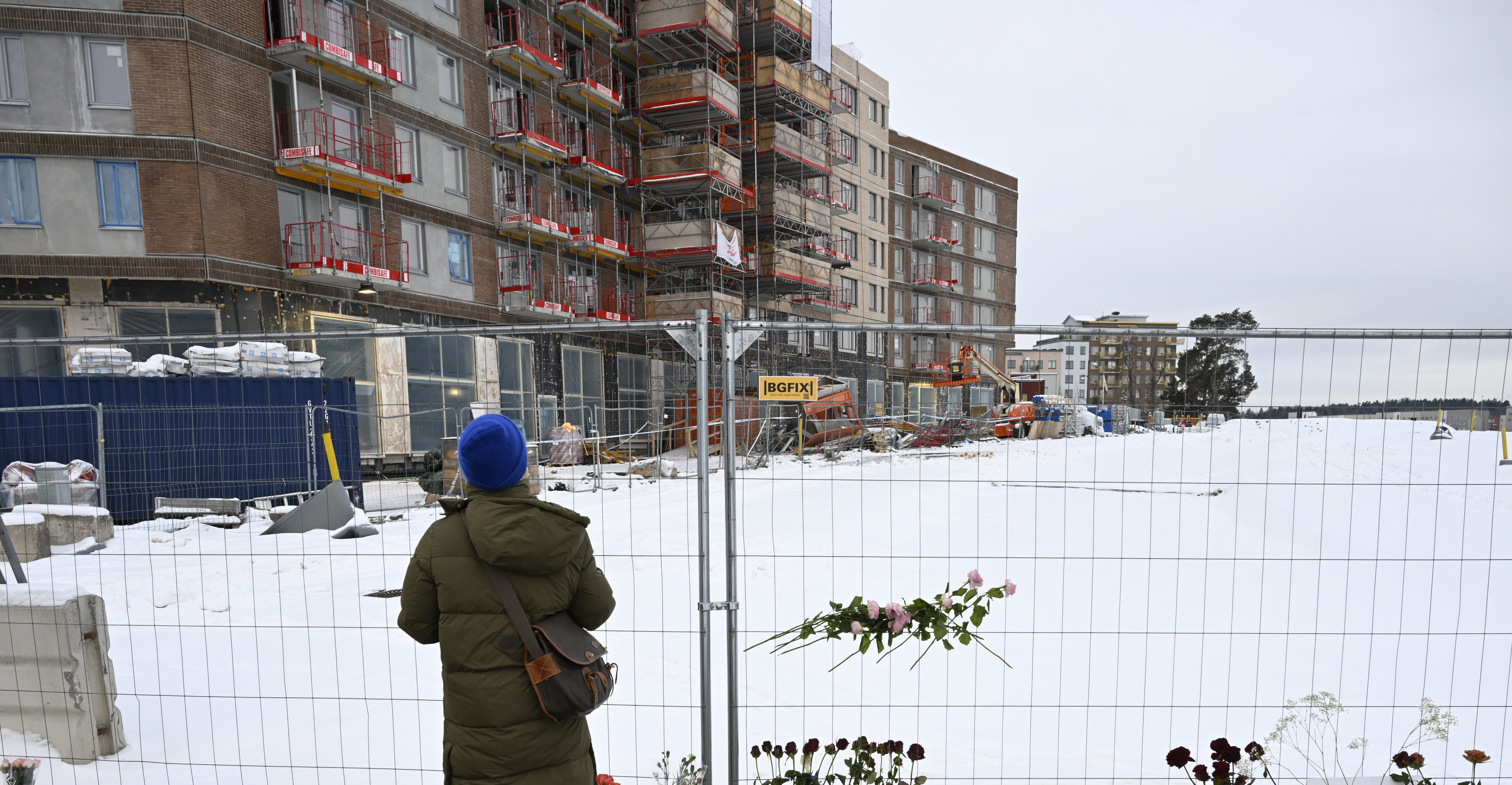 En kvinna står framför ett staket med blommor.
