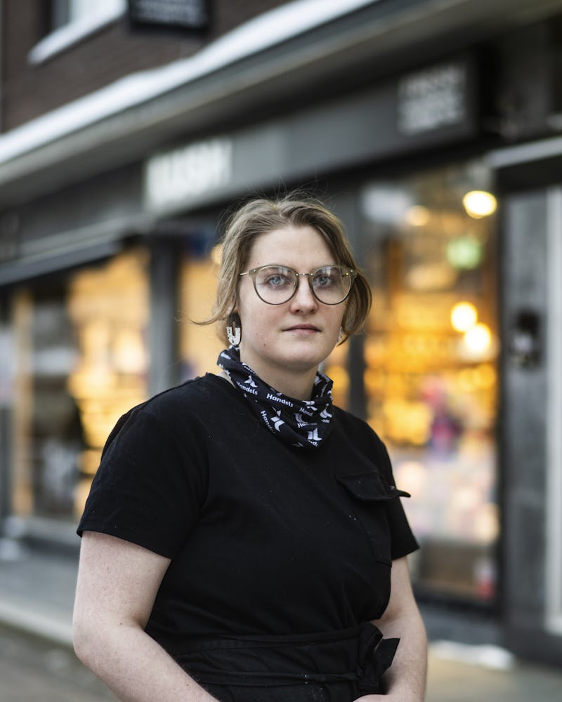 En person som bär glasögon och ett förkläde som står framför en butik.