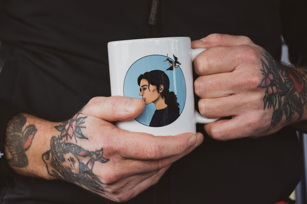 Närbild på ett par händer som håller en mugg med en målning av sjömannen Annie, en karaktär skapad av Emily Gyllenspetz.