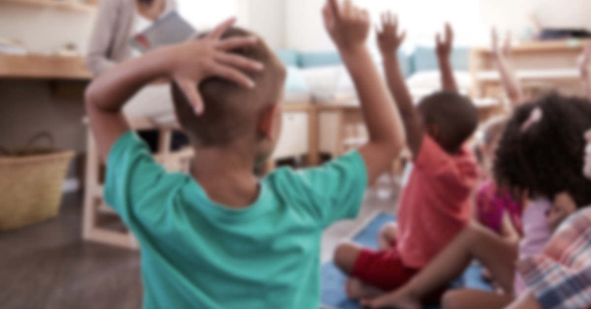 En grupp barn i en förskoleklass som räcker upp händerna.