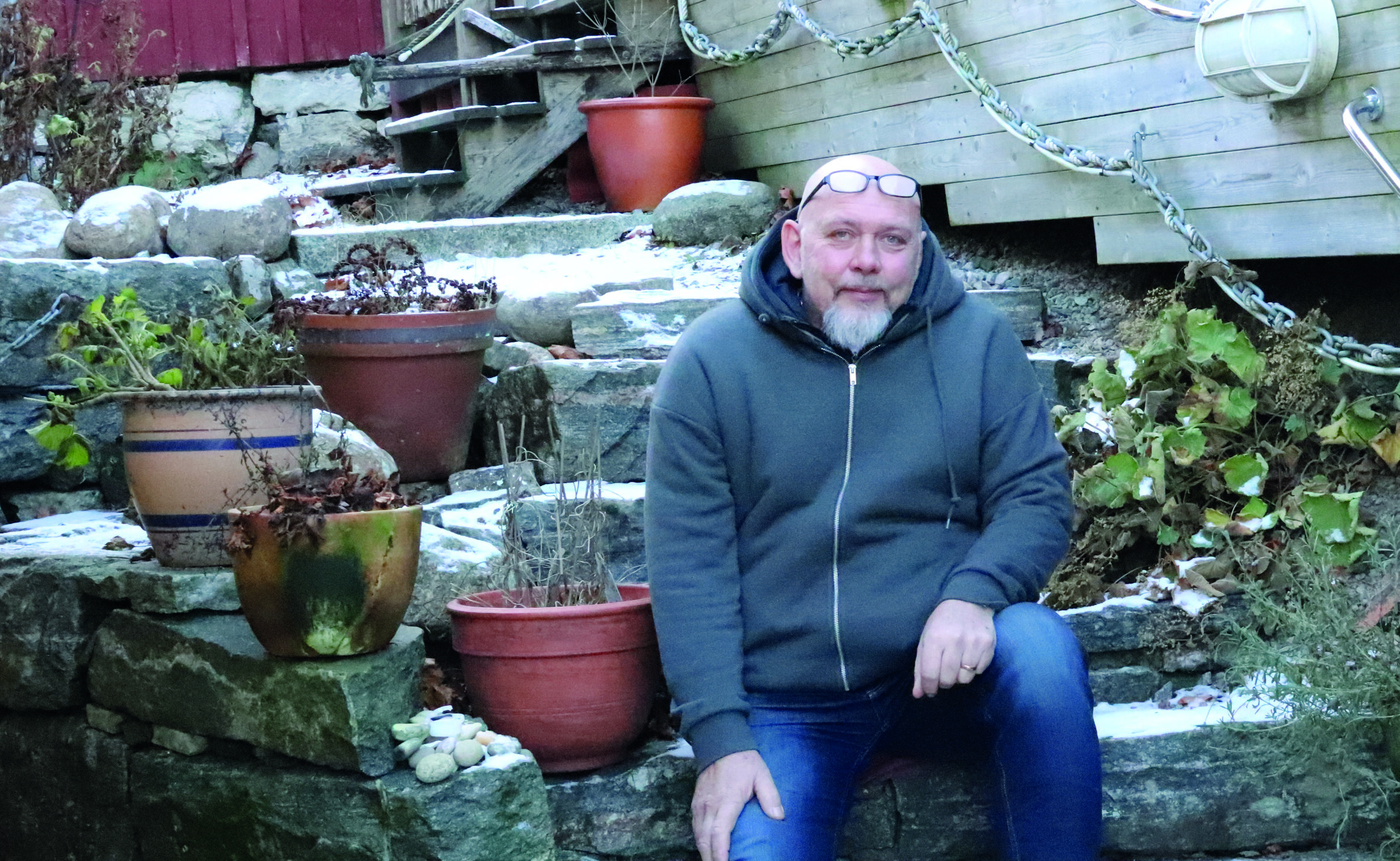 Henric Andersson som sitter på trappan till ett hus med krukväxter.