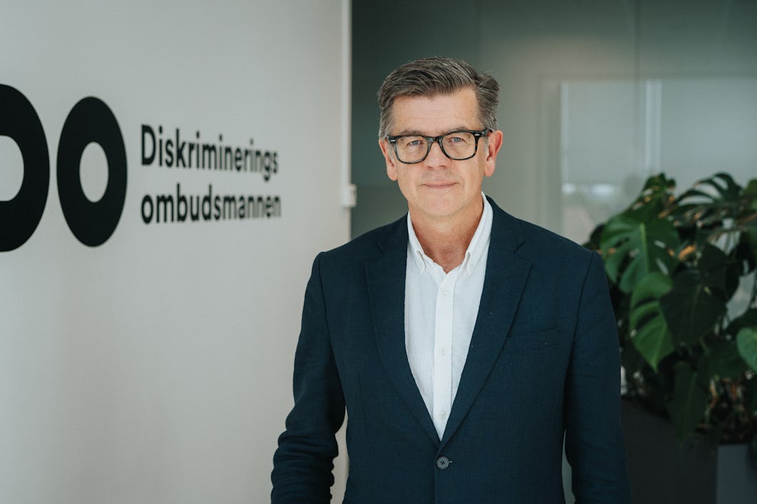 Porträtt på Lars Arrhenius i kavaj bredvid en vägg där det står ”DO Diskrimineringsombudsmannen”.