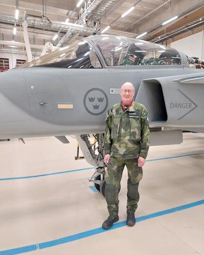 Lars Bäckström, flygtekniker på Försvarsmakten, står i kamouflagekläder framför ett stridsflygplan.