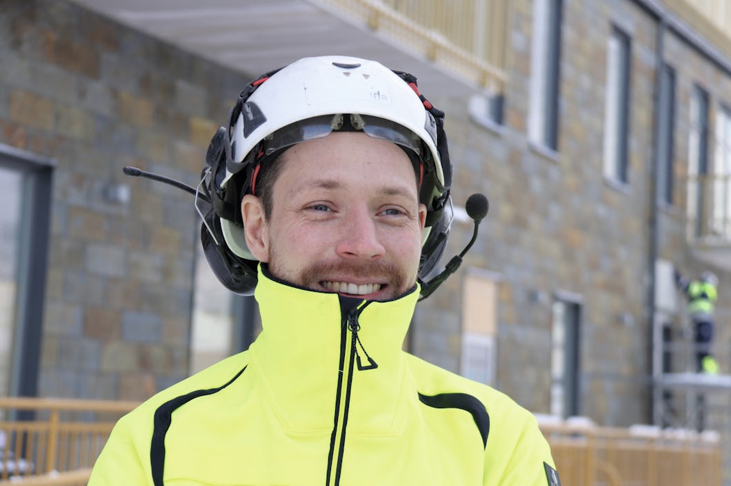 Marcus i en gul jacka som ler framför en byggnad.