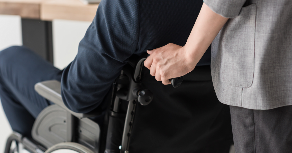 En man i en rullstol som leds fram av en kvinna.