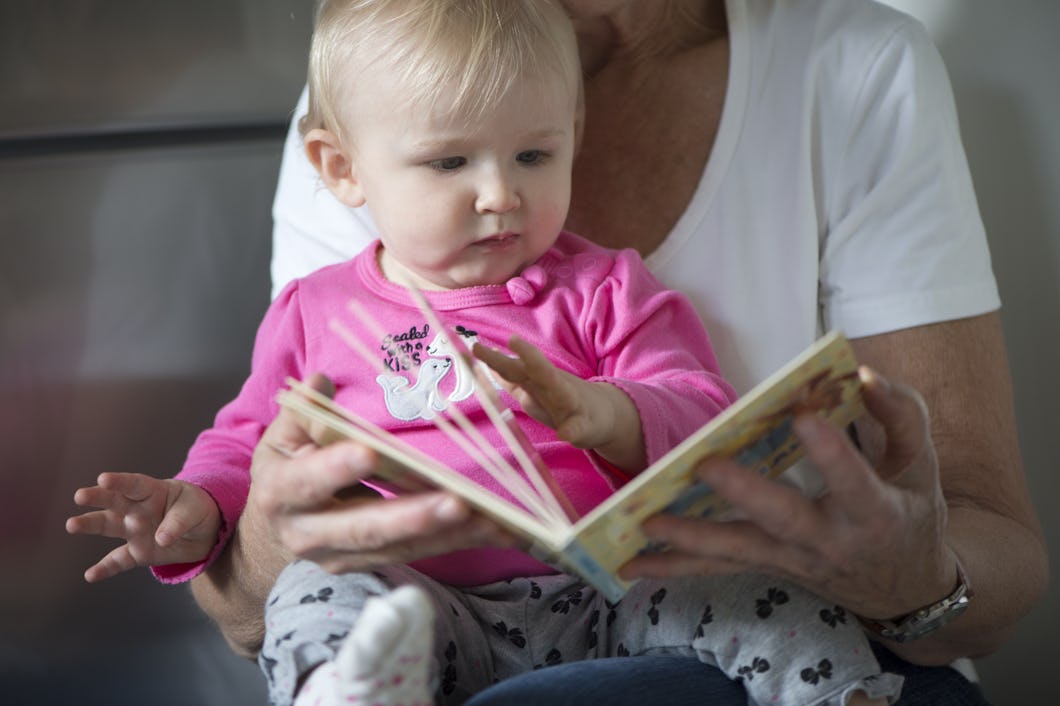 En äldre person som läser ur en bok för en bebis.