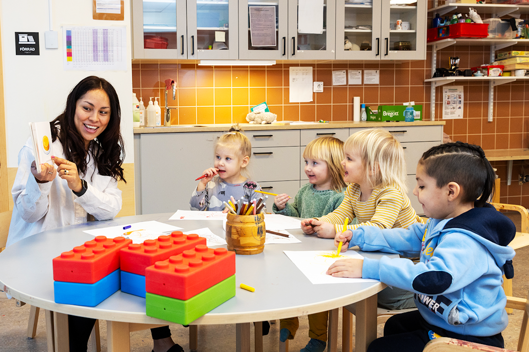 Specialistbarnskötare Daglem Nilsson på Munktellstadens förskola i Eskilstuna visar en bok för en grupp barn som sitter runt ett bord.