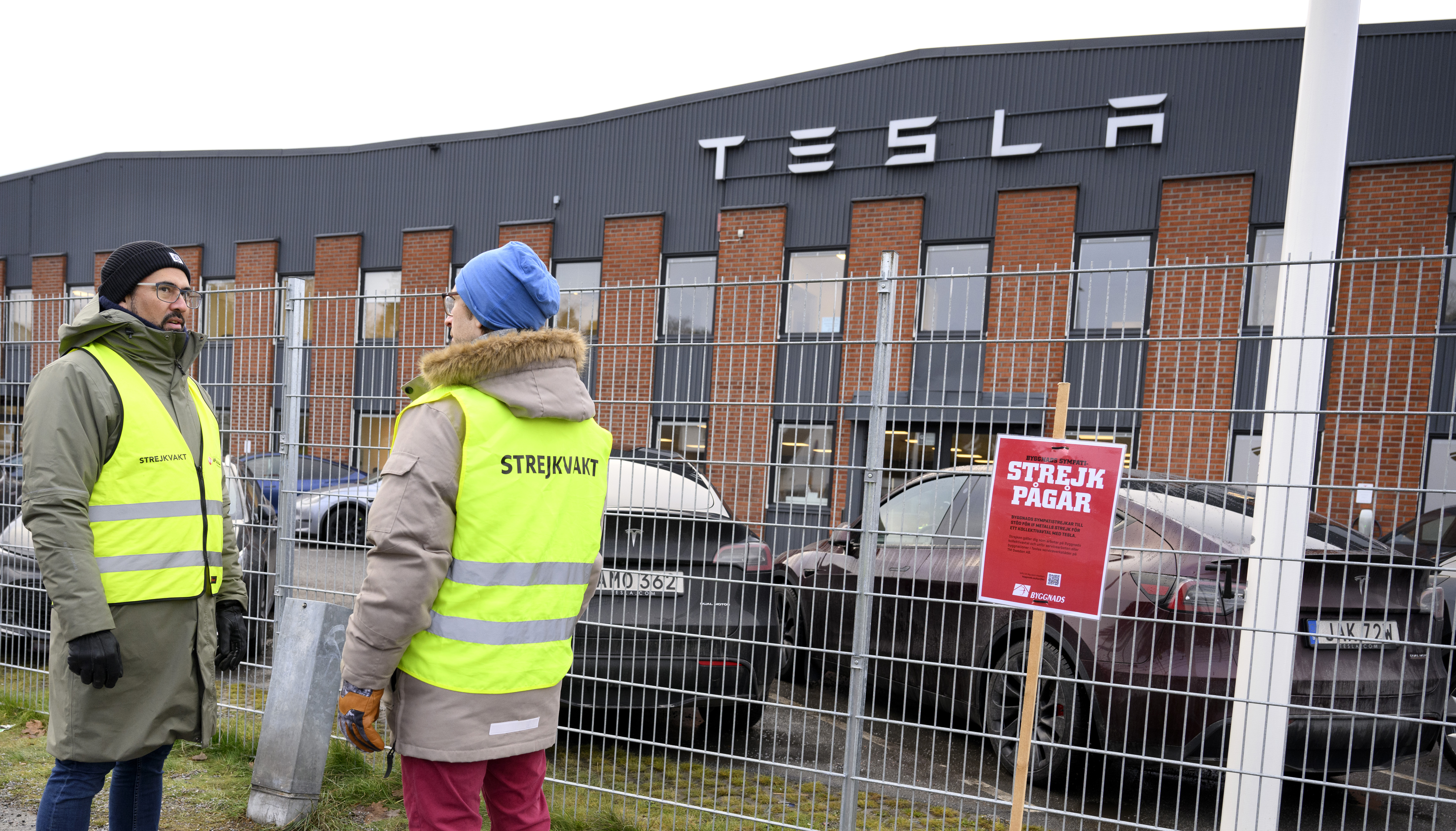 Strejkvakter står utanför stängsel utanför Tesla.
