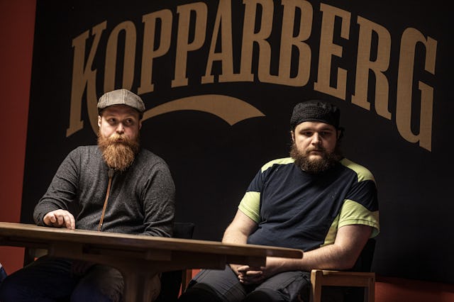 Två män sitter vid ett bord framför en Kopparbergsskylt.