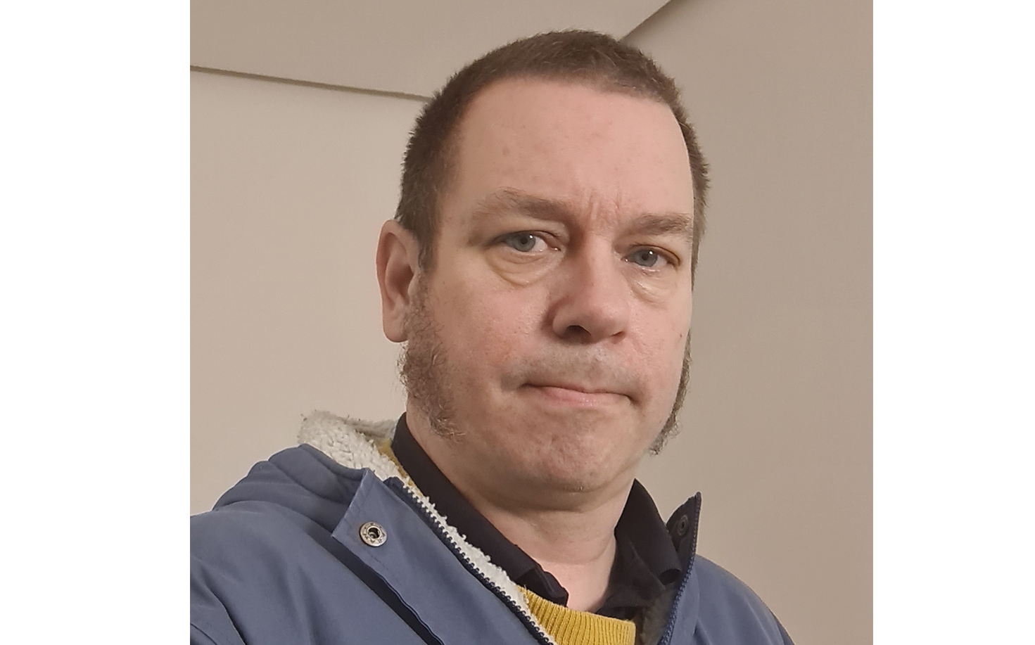 En man i en blå jacka tittar på kameran.