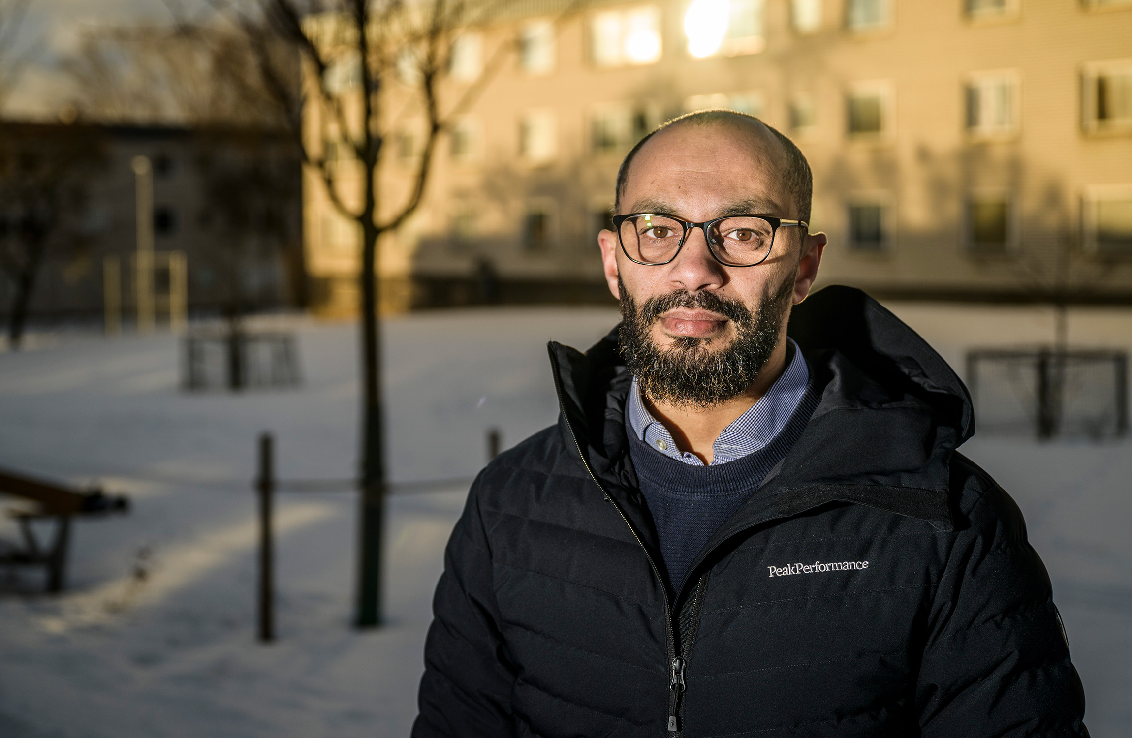 Porträtt på Bader utomhus. I bakgrunden syns en skola där solen blänker i fönstren.