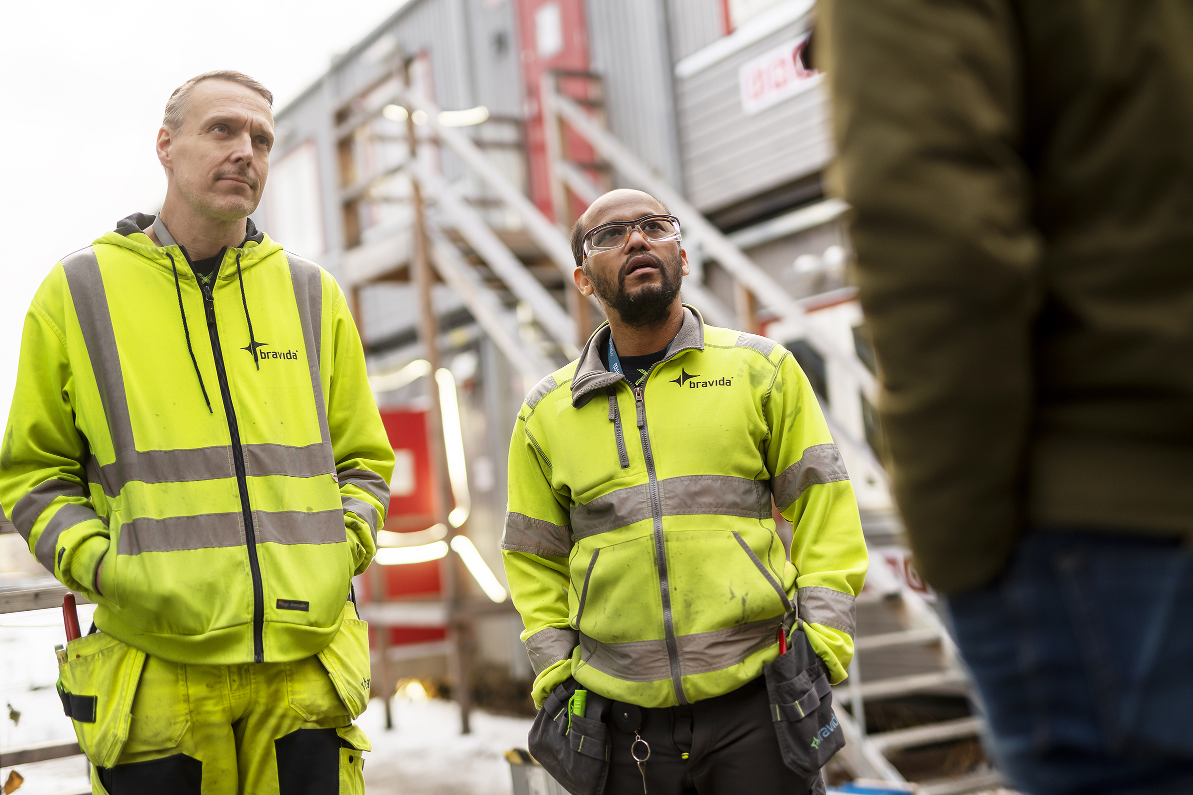 Män i gula västar som står framför en byggnad.