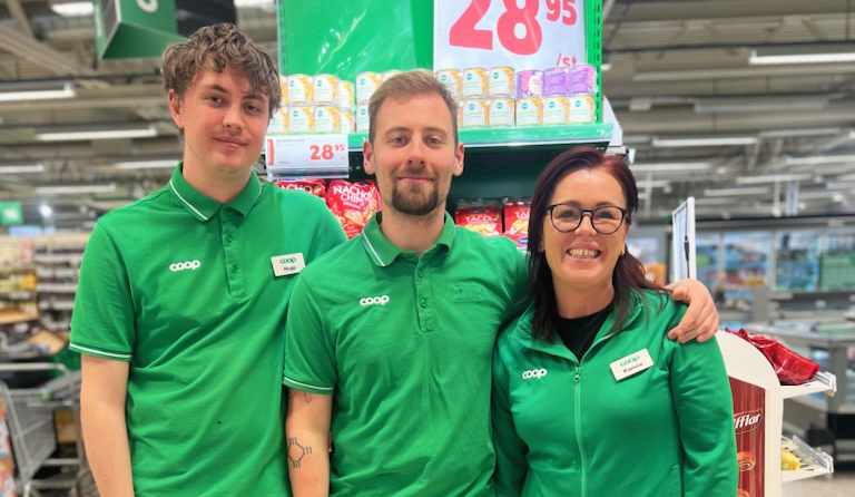Tre personer i gröna skjortor som står bredvid varandra i en Coop-butik.