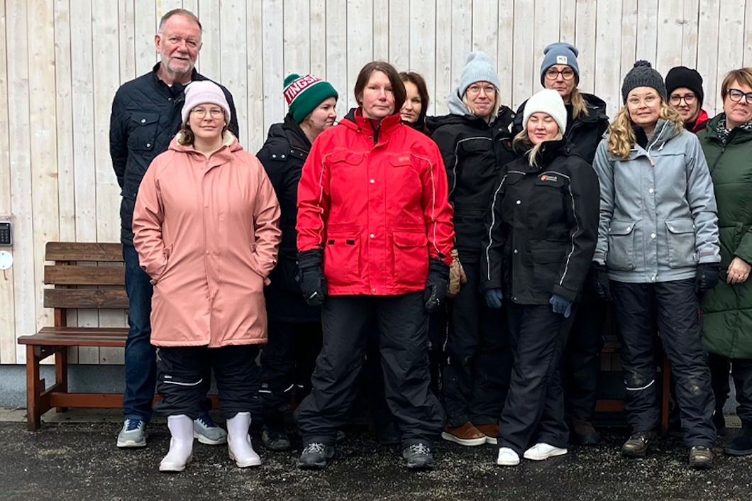 En grupp som jobbar på en förskola poserar framför en byggnad.