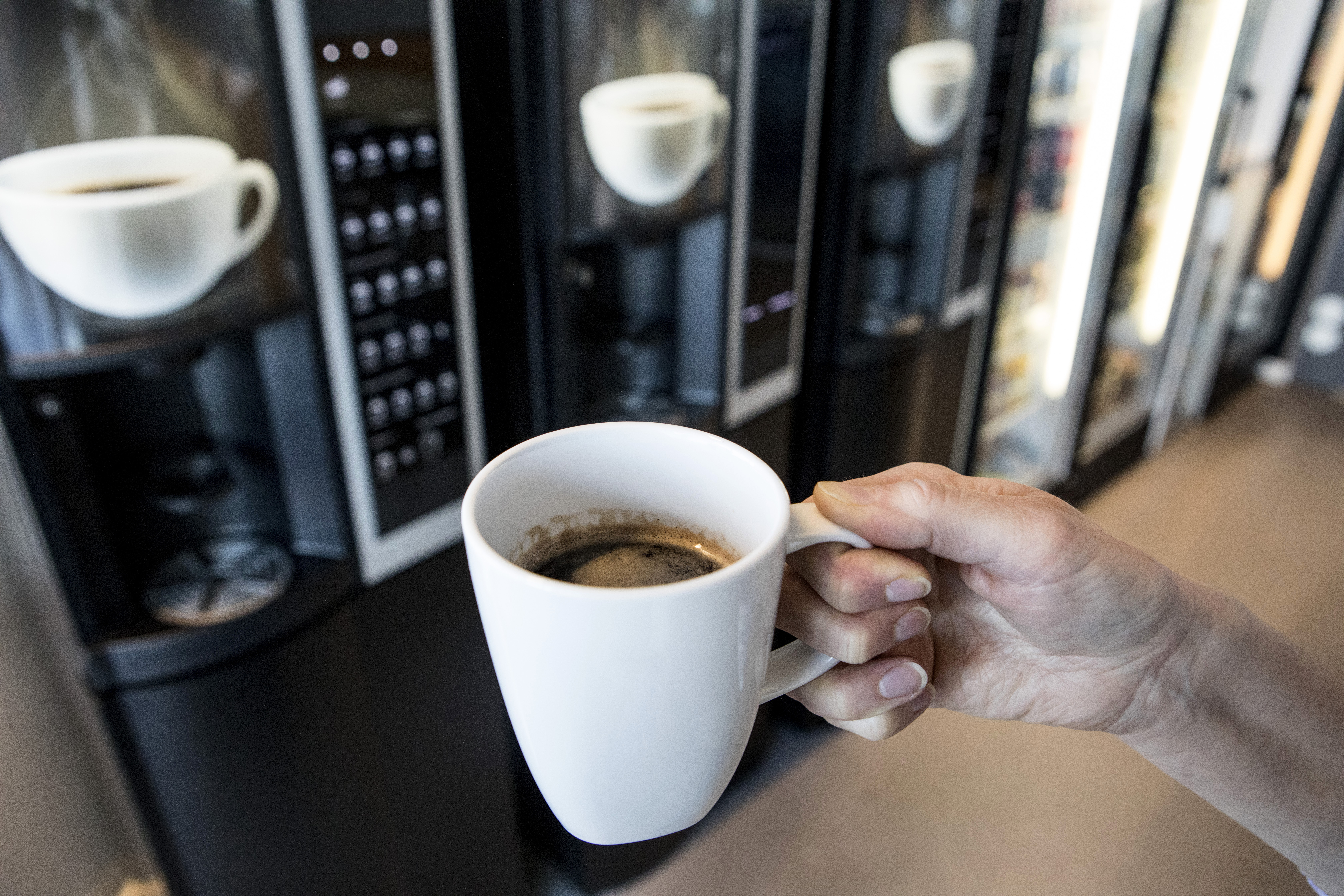En person håller en kopp kaffe framför en kaffeautomat.
