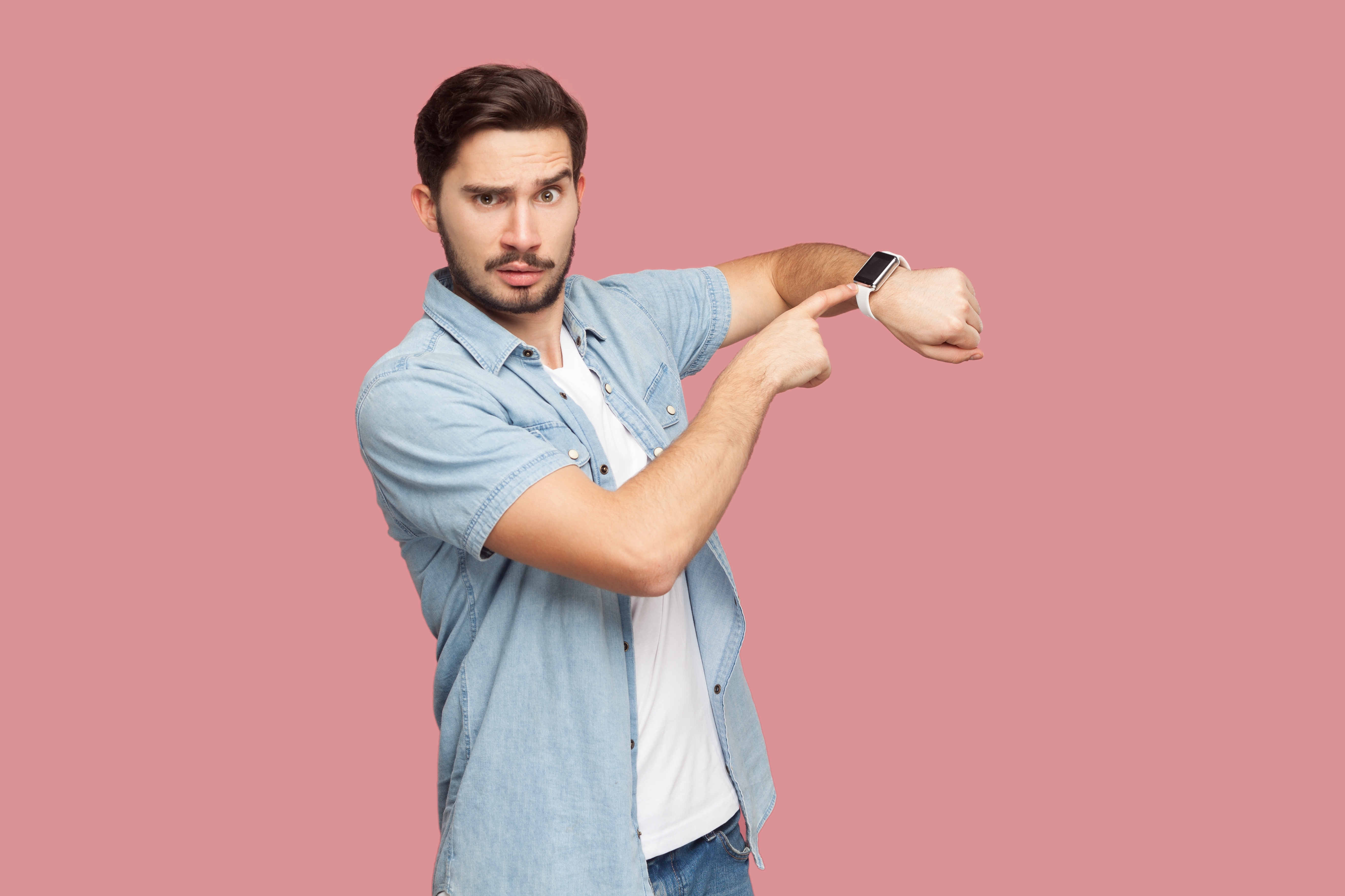 Man med irriterad uppsyn pekar på klockan för att visa att någon är försenad.