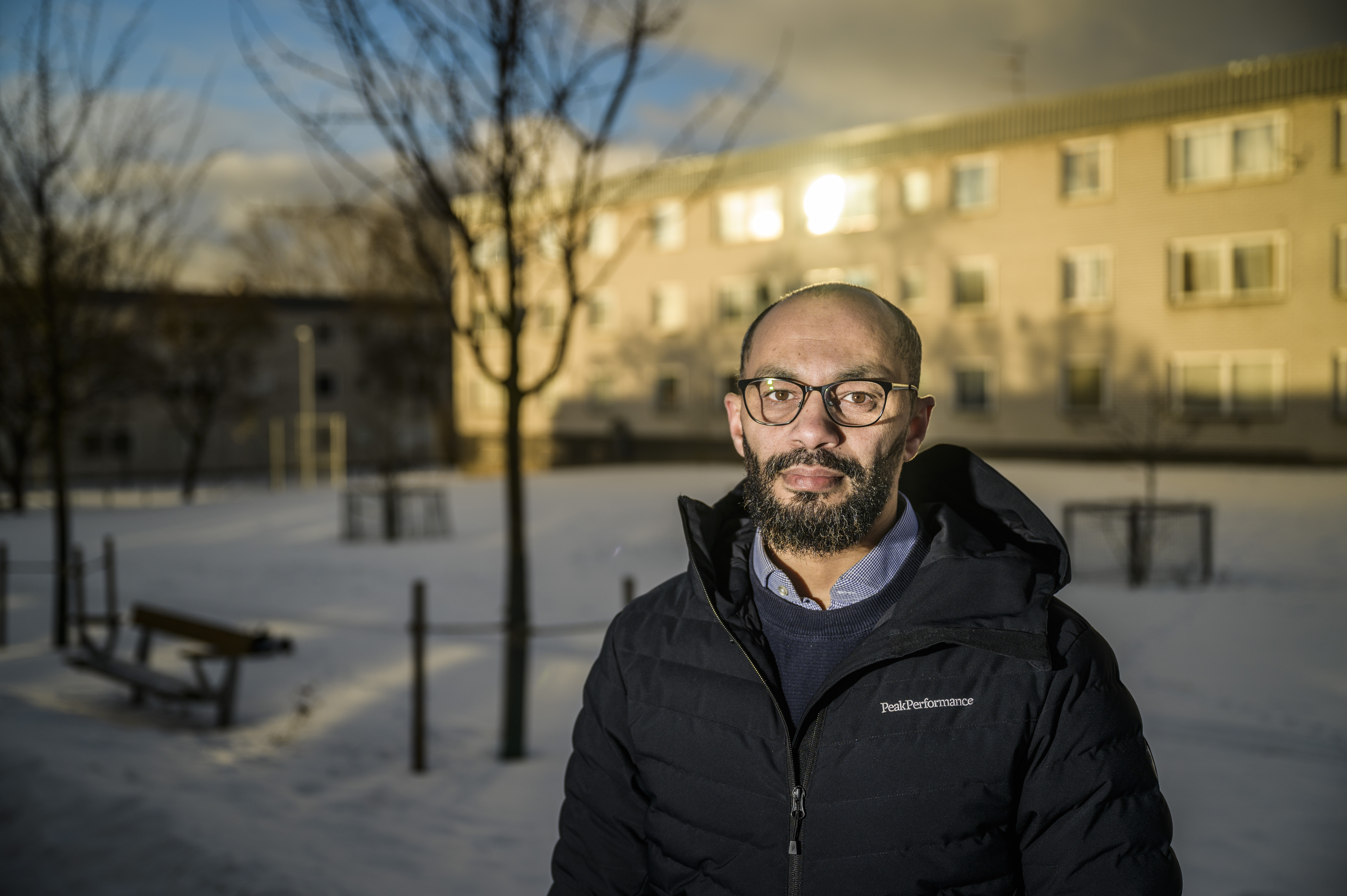 Porträtt på Bader utomhus. I bakgrunden syns en skola där solen blänker i fönstren.