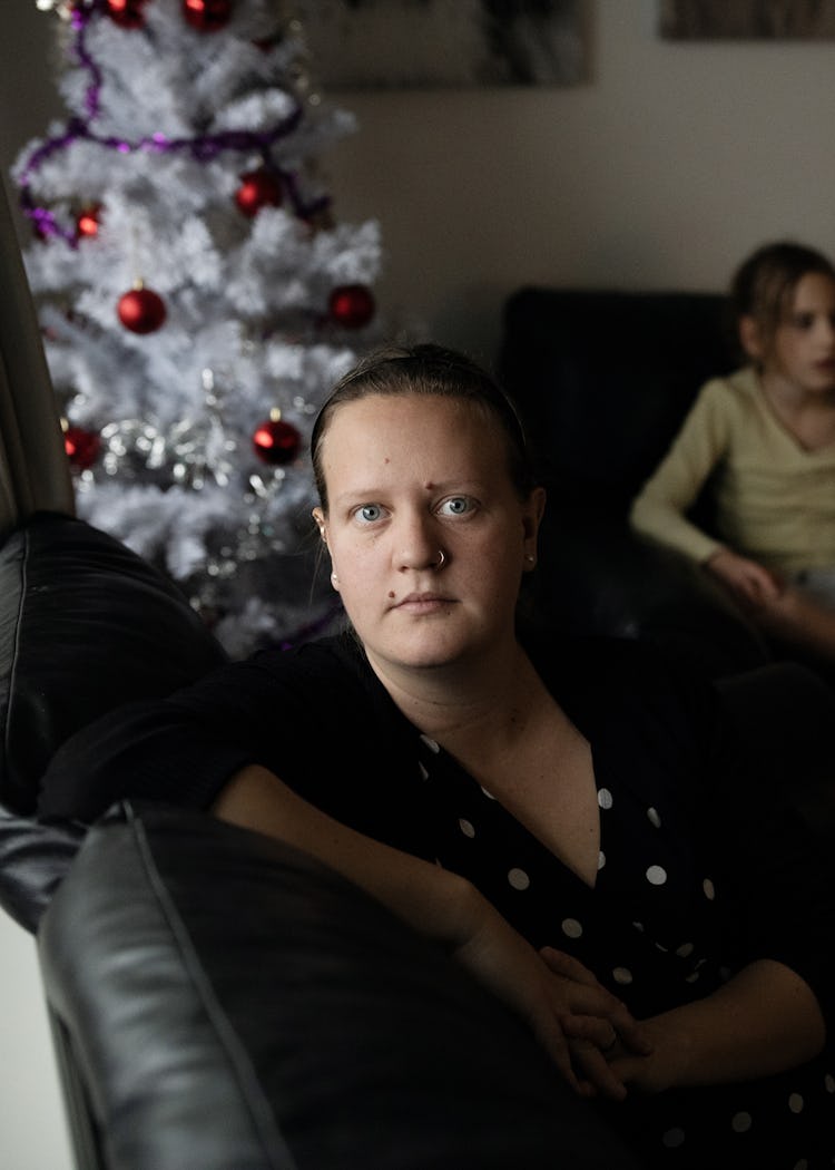 Jennifer Blomberg hemma i lägenheten. I bakgrunden sitter hennes tre största barn och en man i en soffa bredvid en julgran.