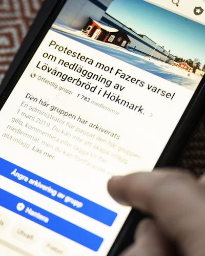 Gunilla som visar Facebook-grupp på en smartphone om en protest vid en fazer-produktionsanläggning.
