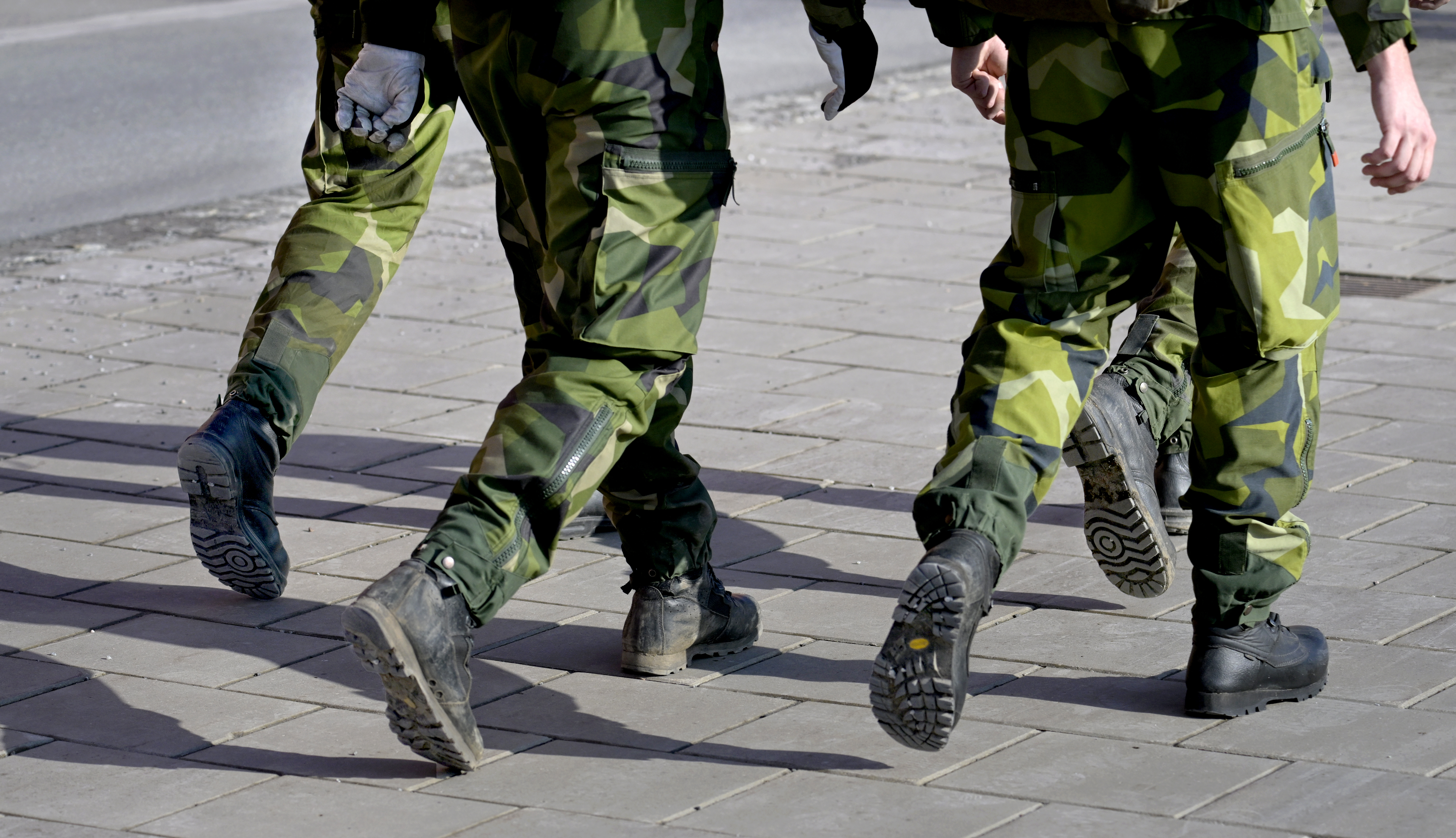 Uniformerade individer marscherar på en asfalterad yta.