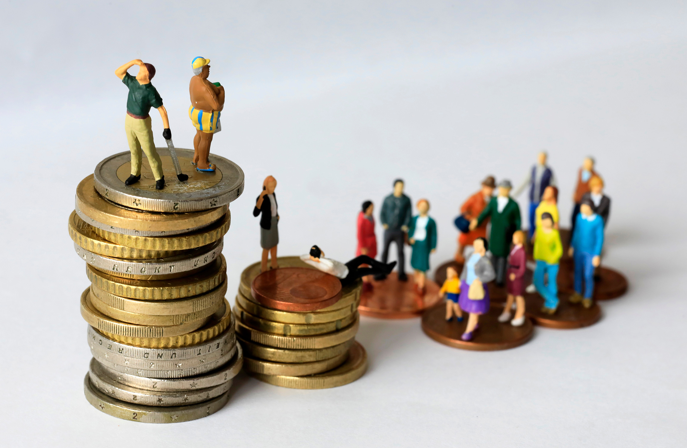 Miniatyrmänniskor som står ovanpå högar av mynt.