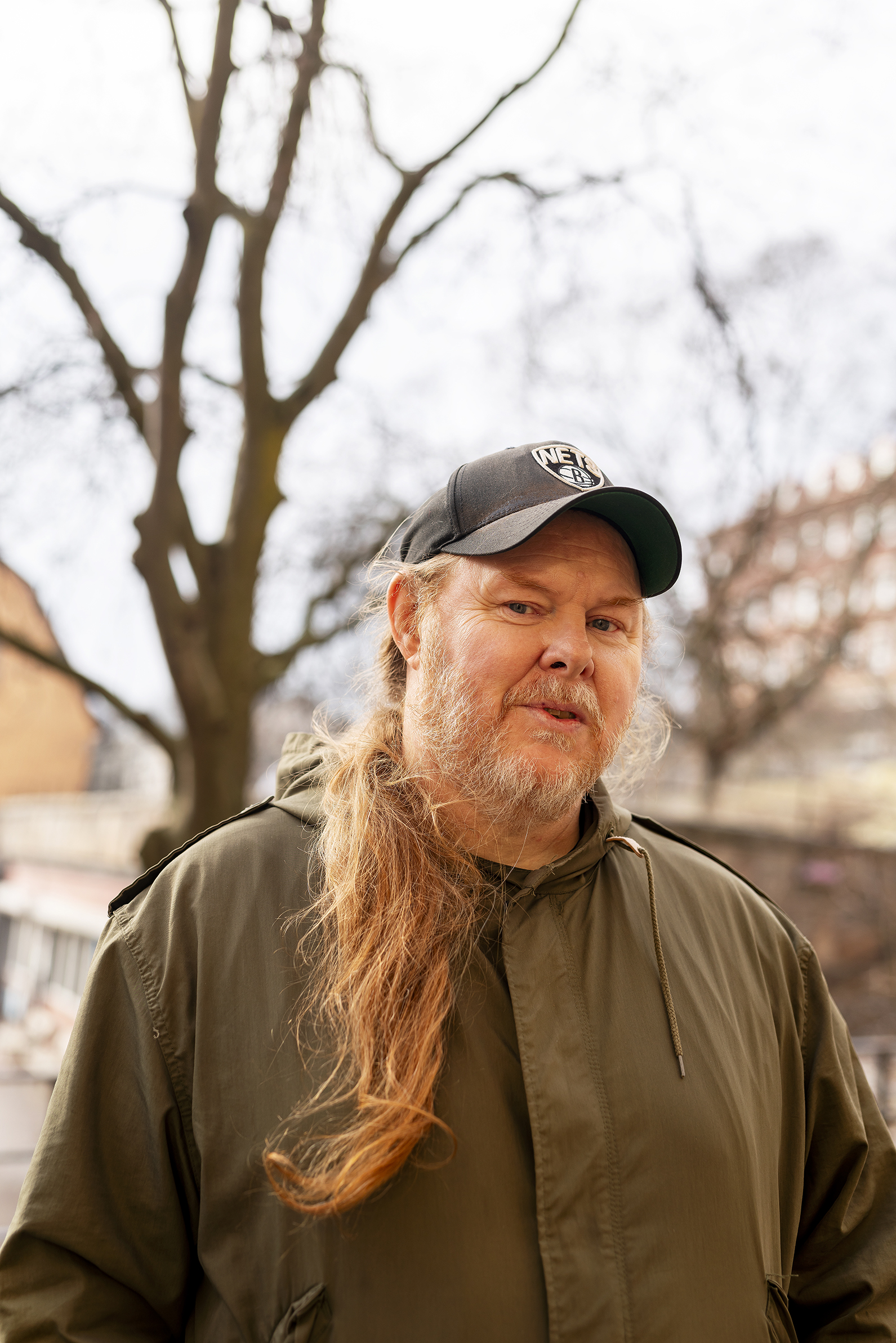 Man som bär en keps och en jacka, står utomhus.