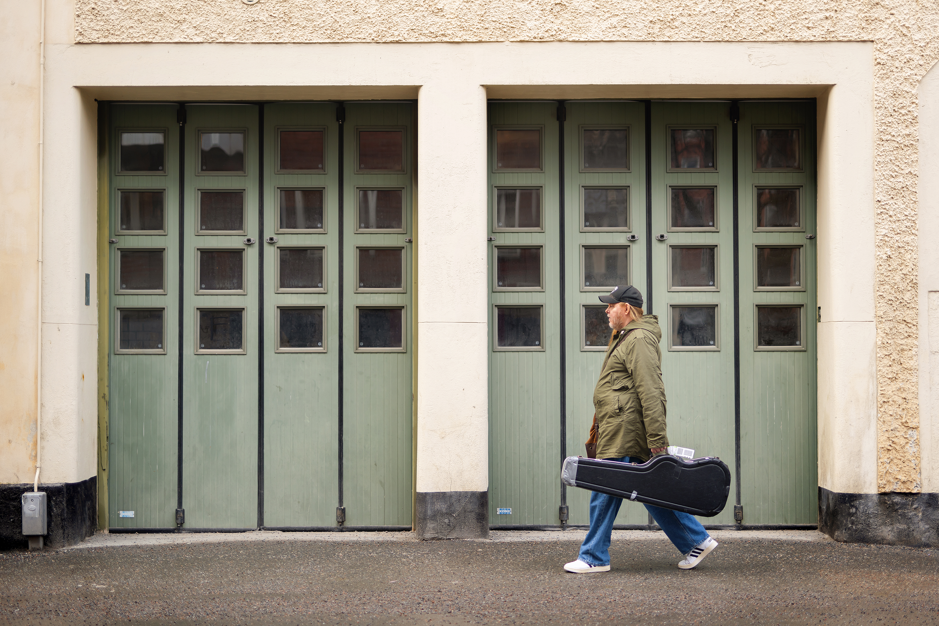 Man går förbi gröna dörrar med ett gitarrfodral.