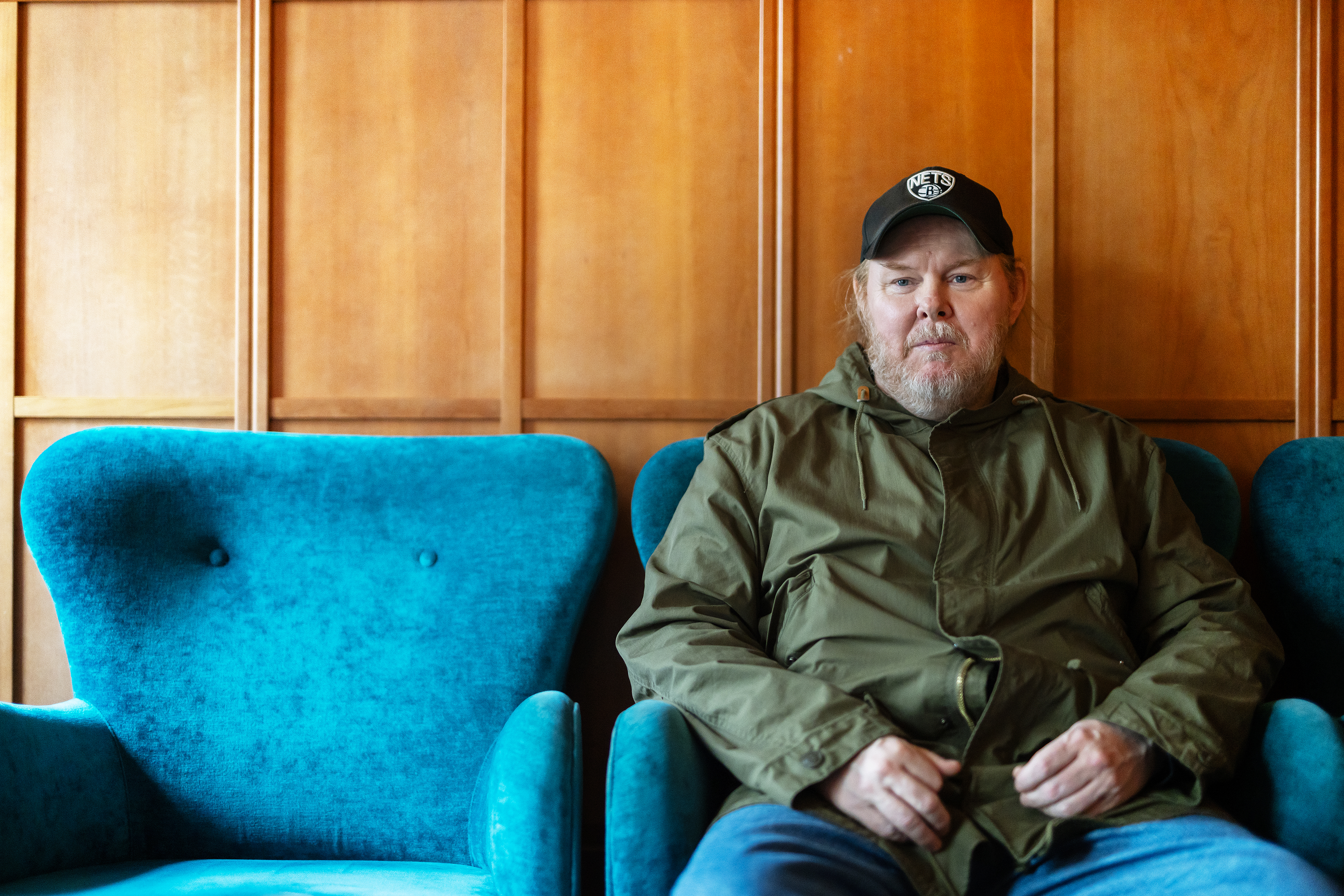 Man sitter i en blå fåtölj mot en träpanelvägg.