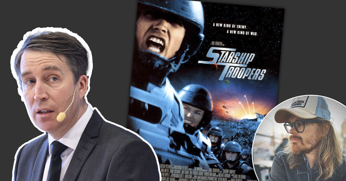 En man i kostym som står bredvid en filmaffisch.