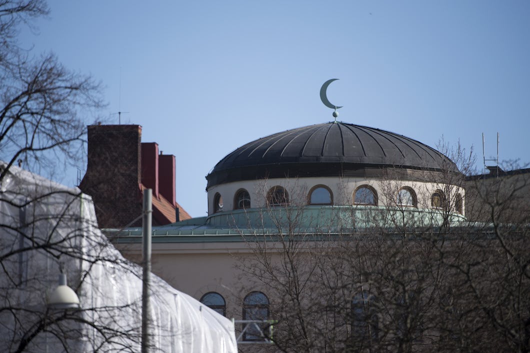 Kupol av en moské med en halvmåne synlig mot en klar himmel, inramad av omgivande byggnader och träd.