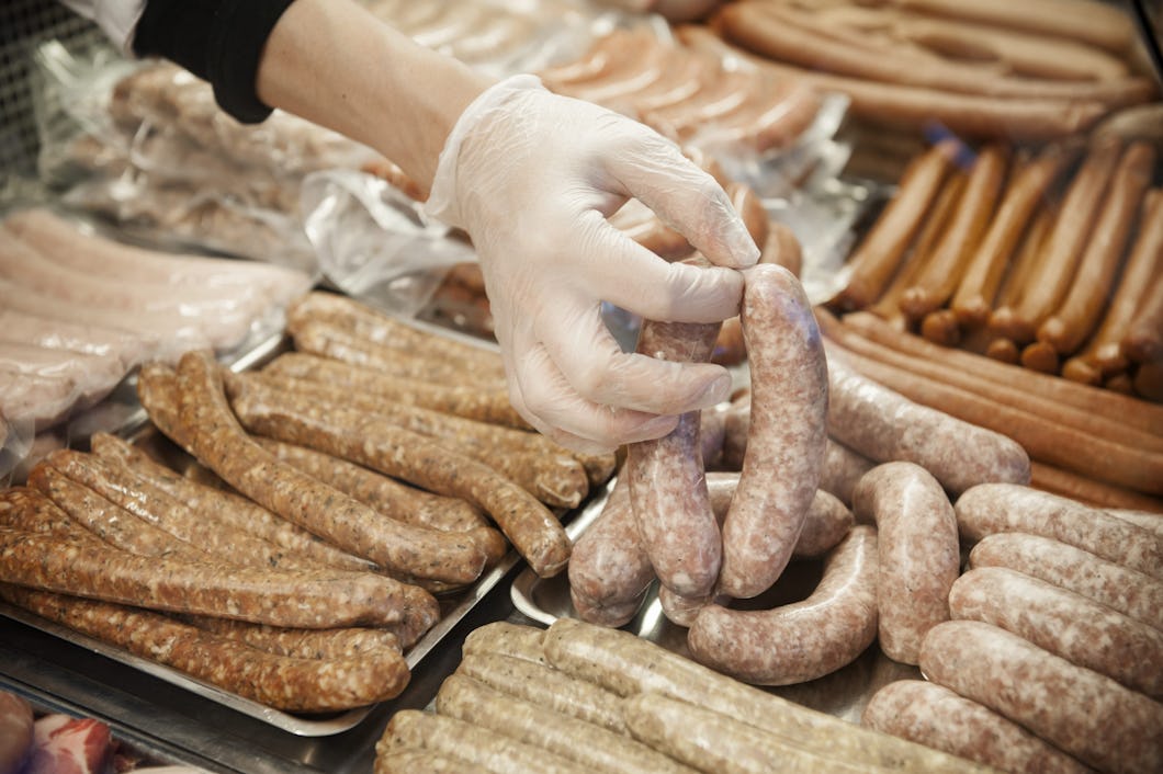 En hand med plasthandske som ordnar olika typer av korvar vid en köttdisk.