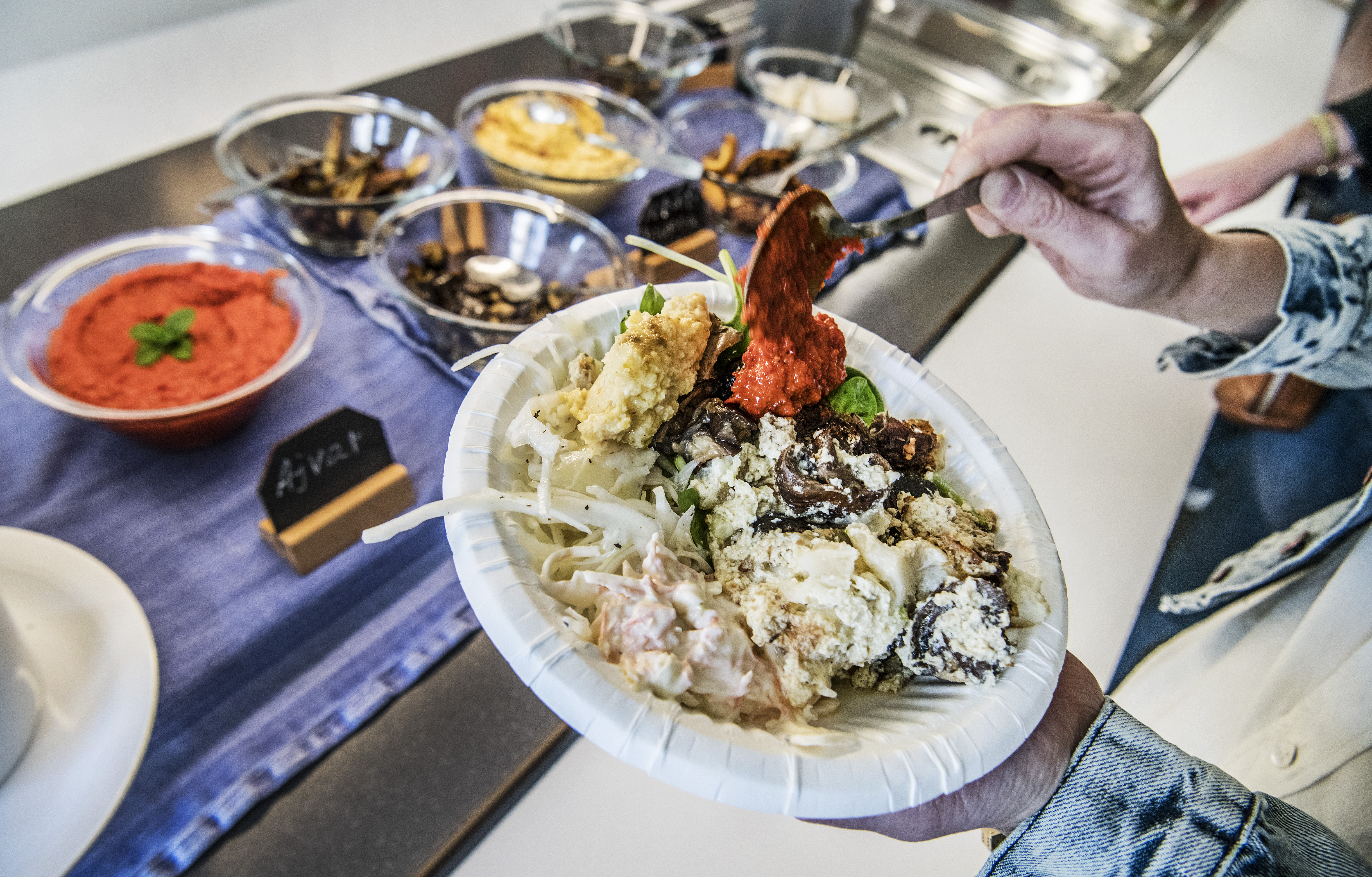 En person som håller en tallrik med mat framför en buffé.