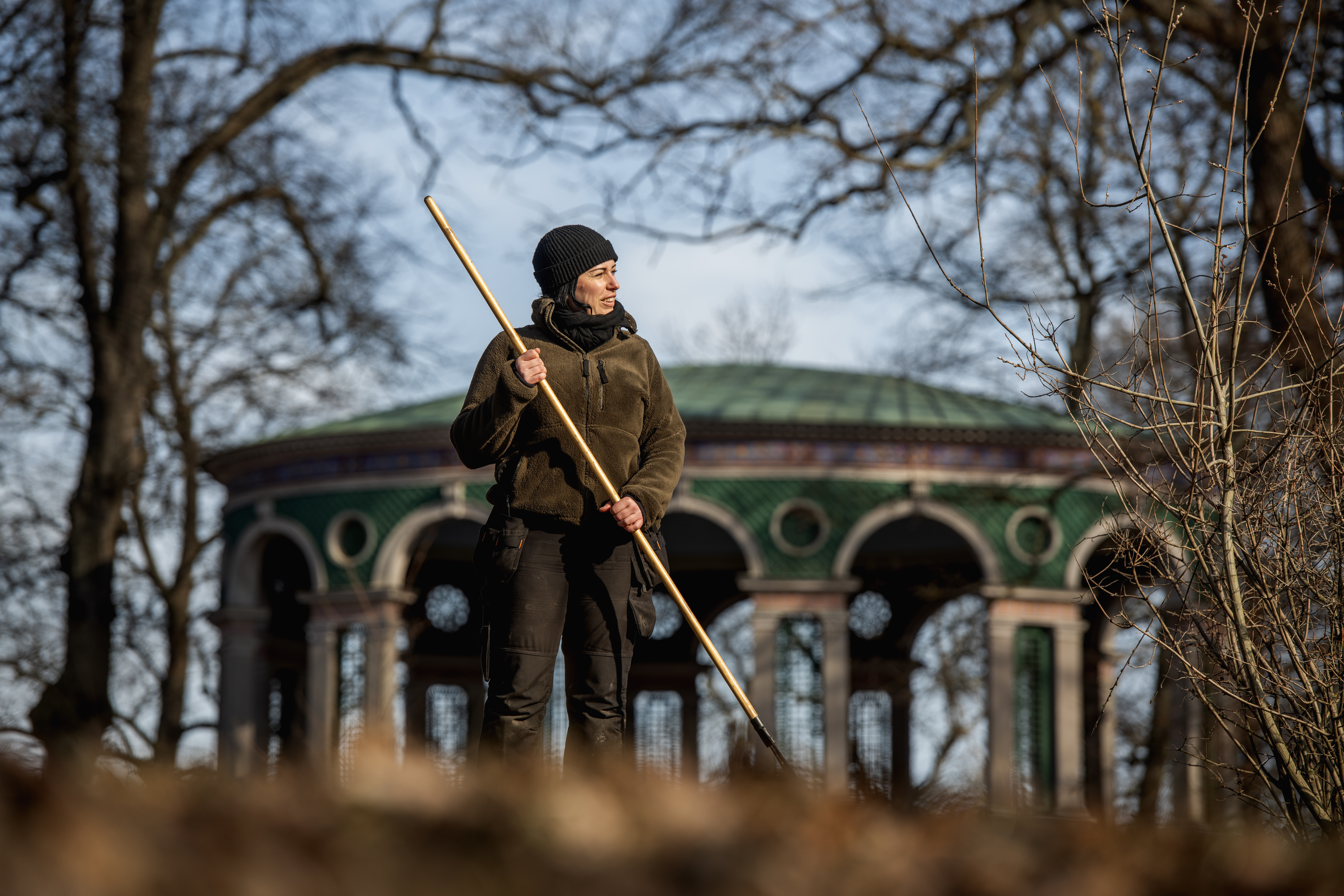 Carolina Mellblom räfsar löv med en grön paviljong i bakgrunden.