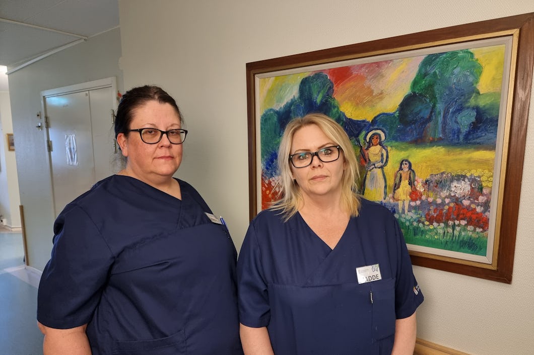 Maria Waidi med mörkt hår och Madelene Pärson i ljust hår iförda scrubs står framför en tavla.