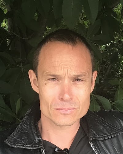 Wallentin Berggren med ett förbryllat uttryck som står framför grönt lövverk.