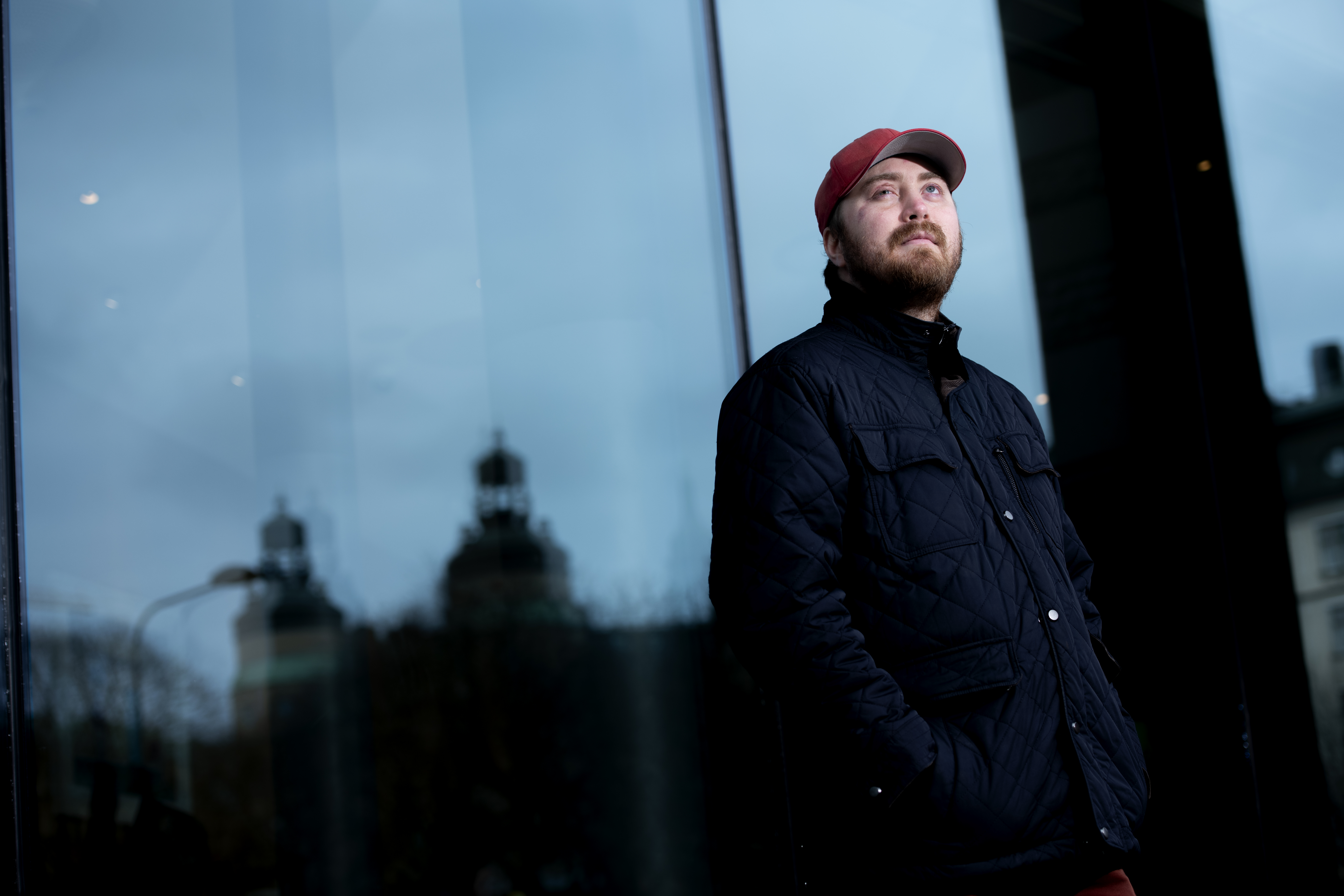 Person med röd mössa och blå jacka står bredvid en glasbyggnad och tittar uppåt.