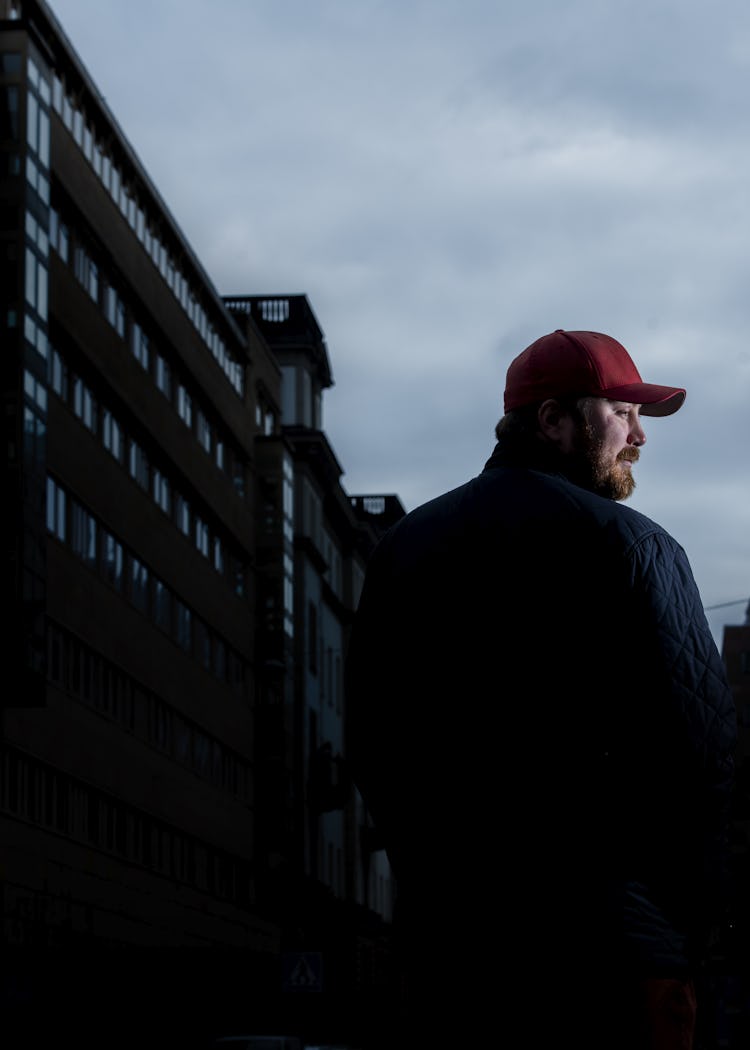 Baloo Beckman med röd keps står i silhuett framför stadshus under molnig himmel.
