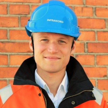 Fredrik Lithner i orange reflexjacka och blå skyddshjälm framför en tegelvägg.